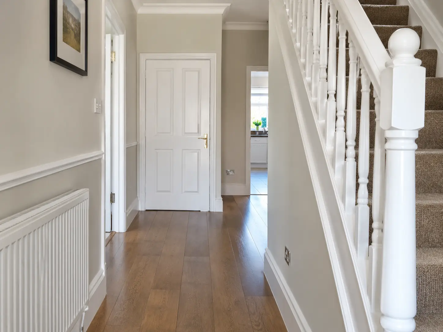 Hallway after repairs: wall made good and painted, new white panelled door and freshly painted stair spindles